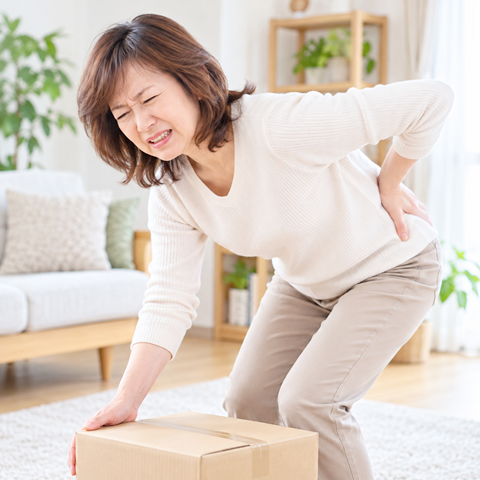 荷物を持ち上げようとして腰に痛みを感じる女性のイメージ